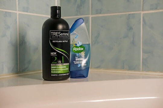 Norwich, Norfolk, UK - November 29 2020. An illustrative editorial photo of a bottle of TRESemme 2 in 1 hair shampoo and conditioner and a bottle of Radox shower gel on the side of a white bath