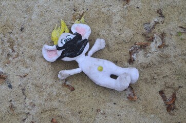 Photo of a child's toy, the face of which is covered with a black mask thrown into the sand.