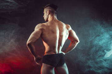 Athletic man flexing muscles in studio on dark background with smoke. Strong bodybuilder with perfect abs.