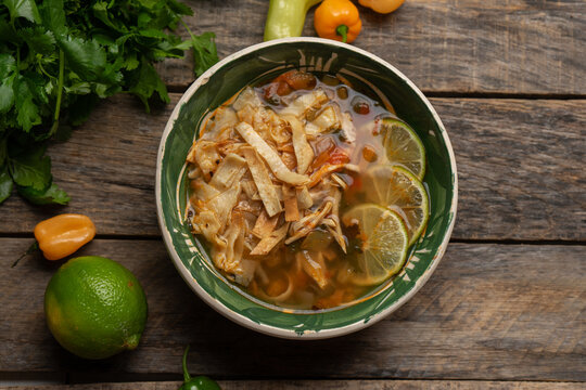 Mexican lime soup with chicken on wooden background