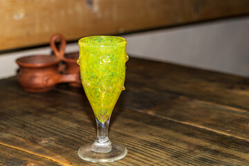 A green wine glass sits on a wooden dining table. Beautiful wavy art glass. Blurred background.