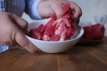 woman at home in the kitchen cuts an appetizing piece of poultry meat into slices with a porcelain knife, raw turkey drumstick, concept of cooking homemade food