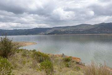 stunning summer andean lake scene with green mountains and green trees at sunny white cloudy day.