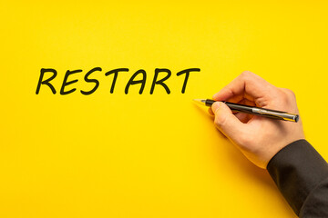 Male hand writes in black pen the word restart on a yellow background with copy space. Business concept photo