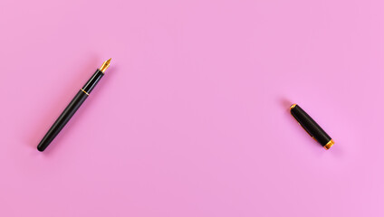 Top down view - black fountain ink pen with gold nib, opened, cap on the right, pink background,...