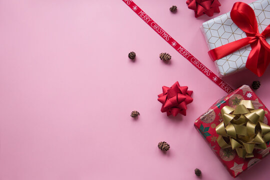 Christmas pink background with gifts, presents, 
wrapped boxes, pine cones and Christmas ribbon with the letters Merry Christmas. Flat lay view with free space 