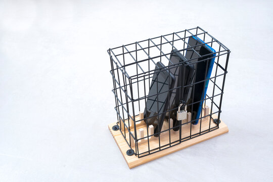 three smartphones locked in a cage with a padlock, concept of social isolation or phone abuse and social networks, white horizontal background