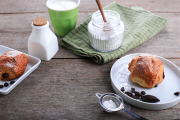 Fresh Baked Chocolate Croissants (Pain au Chocolat) with Milk for Breakfast. Served on White Plate on Rustic Table Copy Space for Text