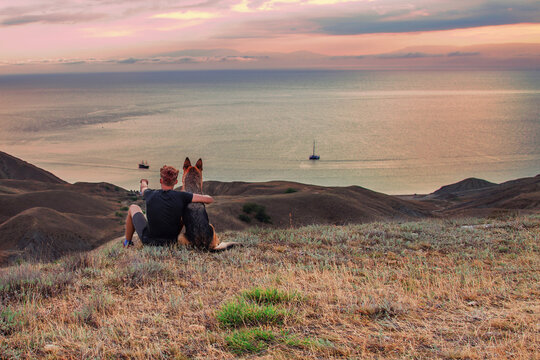  young man and german shepherd dog looking at ships on sunset. Togetherness and Friendship Concept. Trekking, travel and activity concept. Recreation and healthy lifestyle outdoors. Social Distance.