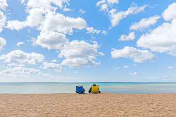 A couple comfortably sitting in beach chairs enjoying undisturbed view at quiet and calm sea waters.