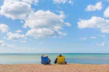 A couple comfortably sitting in beach chairs enjoying undisturbed view at quiet and calm sea waters.