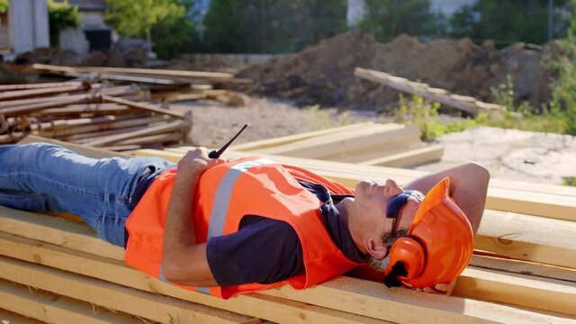 Middle-aged foreman laying down for a nap at construction site while have a break he wearing protective uniform and goggles holding his working ration