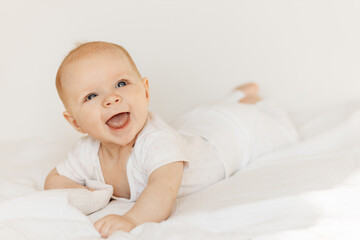 Portrait of beautiful baby girl laying on comfortable bed at home, wonderful cute toddler look around with big interest, smiling, childhood and childcare concept