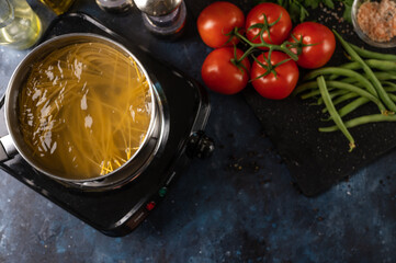 Top view of spaghetti cooking process on marble dark blue table with variety of ingredients background. Backstage of cooking pasta. Close-up view. Cookbook design.