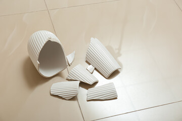 Broken white ceramic vase on floor indoors