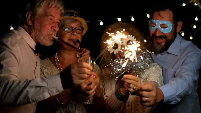 group of four people enjoying new year night celebrating with sparklers in the middle and looking at the camera - adults having fun together