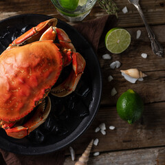 Macro shot of black plate with cooked king crab served with ice cubes. lime and seashells on rustic wooden background. Delicious meal. Seafood concept. View from above. Space for text.