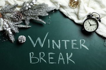 Flat lay composition of Christmas decorations, knitted plaid and alarm clock on school blackboard with phrase Winter Break