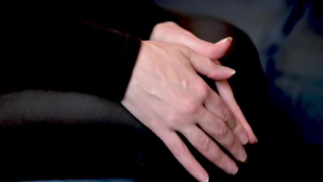 The woman rubs her knee with her hands. A woman is sitting on the couch with knee pain.