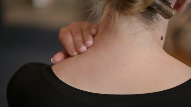 A woman is sitting on the couch with a pain in her neck. The woman rubs her neck.