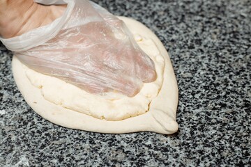 Baker hands preparing khachapuri on kitchen table. cook making traditional georgian treat with raw dough and egg. recipe concept