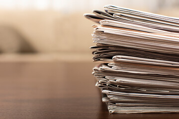 Pile of newspapers lying on the wooden table with blurred background and copy space for text. Close Up of newspapers stack. Journalist concept.