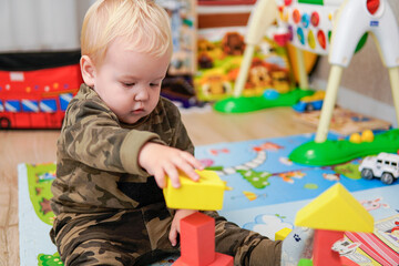 Fototapeta na wymiar Little boy with blond hair builds a house of cubes