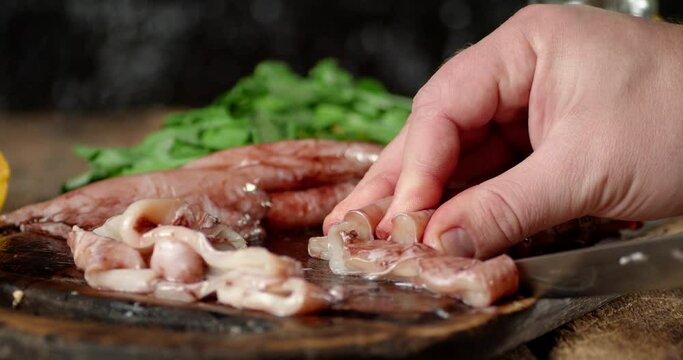 Men's hands cut with a raw squid knife on a cutting board. 