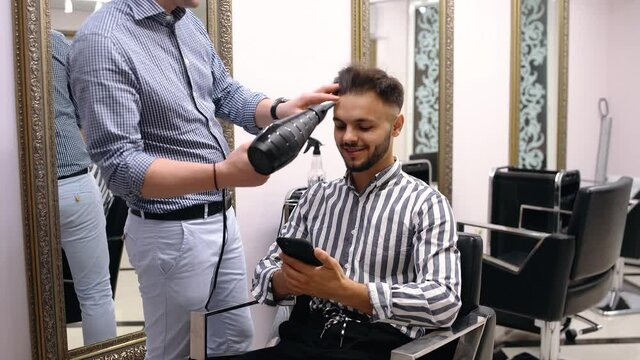 Businessman makes a transaction on the phone, while making a new cutter at the barber shop. Handsome young Caucasian man getting a haircut in a modern salon. Hand-fired. 4K. Reopening of mills after