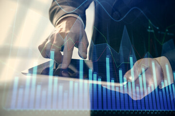 Double exposure of man's hands holding and using a digital device and forex graph drawing. Financial market concept.