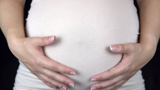 Pregnant woman stroking her big belly with her hands. Woman in a light T-shirt
