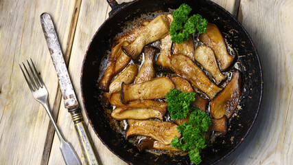 Fried eringi mushrooms in a frying pan on a wooden surface.