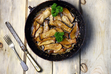 Fried eringi mushrooms in a frying pan on a wooden surface.