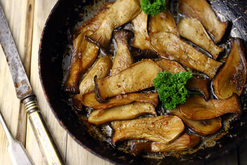 Fried eringi mushrooms in a frying pan on a wooden surface.
