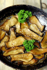 Fried eringi mushrooms in a frying pan on a wooden surface.