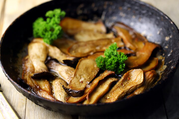 Fried eringi mushrooms in a frying pan on a wooden surface.