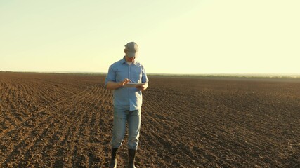 A farmer works with a tablet in a plowed field in sun. agronomist with a tablet studying the...