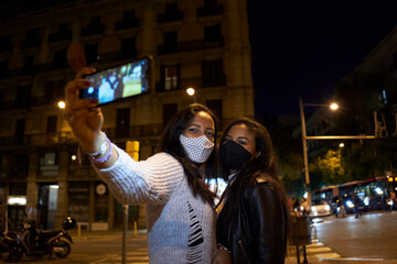 Two black women friends taking a selfie at night in a busy city.