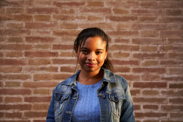 Portrait of an African American black woman looking at the camera smiling in front of a brick wall.