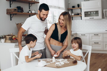 beautiful family preparing breakfast together in the bright kitchen at home. Mom Dad and 2 seven-year-old sons have fun and cook cheese cakes from flour and cottage cheese