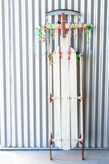 Obraz premium vintage sled decorated with red, green and gold Christmas curling ribbon, leaning against a tin wall with copy space