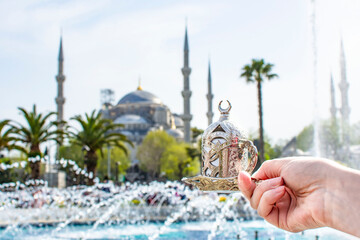 Naklejka premium Woman's hand holding metal cup with Traditional turkish coffee in front of Blue mosque (aka Sultanahmet Camii) in Istanbul, Turkey. Istanbul's main attractions.