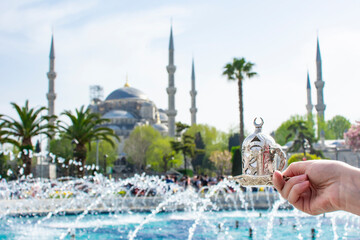 Naklejka premium Woman's hand holding metal cup with Traditional turkish coffee in front of Blue mosque (aka Sultanahmet Camii) in Istanbul, Turkey. Istanbul's main attractions.