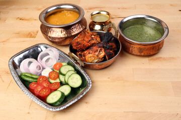 Spicy red Chicken grilled tikka tandoori nan bread green spinach curry yogurt sauce dal tomato cucumber onion salad set in metal stainless steel brass copper pot on light wood background