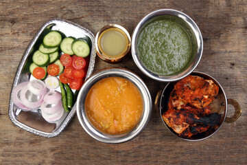 Spicy red Chicken grilled tikka tandoori nan bread green spinach curry yogurt sauce dal tomato cucumber onion salad set in metal stainless steel brass copper pot on rustic vintage wood background