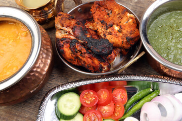 Spicy red Chicken grilled tikka tandoori nan bread green spinach curry yogurt sauce dal tomato cucumber onion salad set in metal stainless steel brass copper pot on rustic vintage wood background