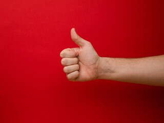 Female hand shows thumb up gesture on a red background