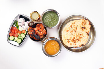Spicy red Chicken grilled tikka tandoori nan bread green spinach curry yogurt sauce dal tomato cucumber onion salad set in metal stainless steel brass copper pot on white background