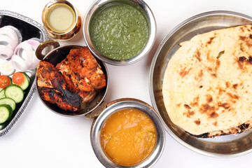 Spicy red Chicken grilled tikka tandoori nan bread green spinach curry yogurt sauce dal tomato cucumber onion salad set in metal stainless steel brass copper pot on white background