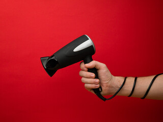 Male hand holding black hairdryer isolated on red background. Hirdresser salon, barber shop, household appliances store concept.